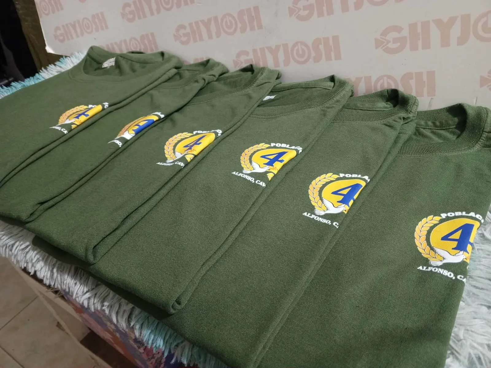 Folded olive shirts with a yellow and blue Poblacion chest mark